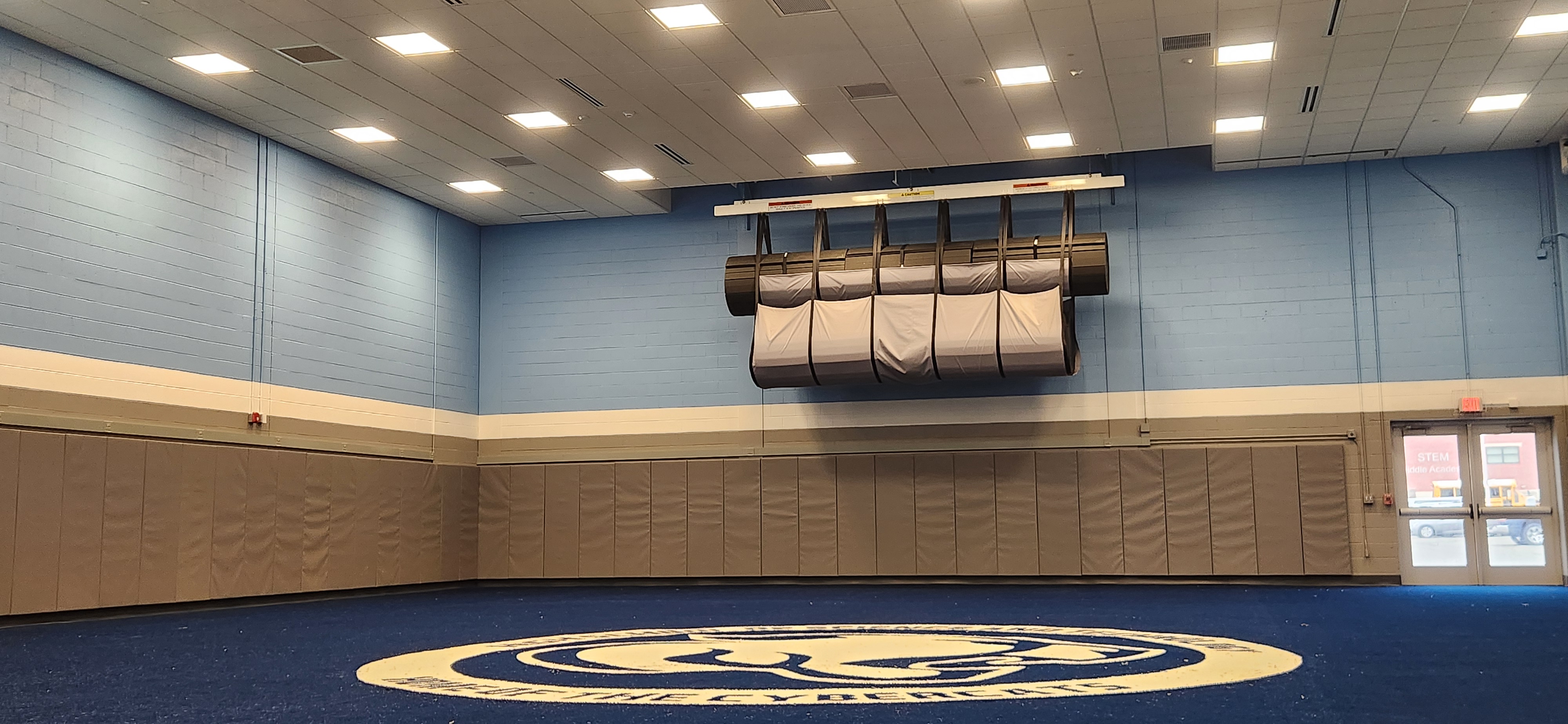 Large indoor court beneath rows of ceiling lights, with a suspended basketball hoop.