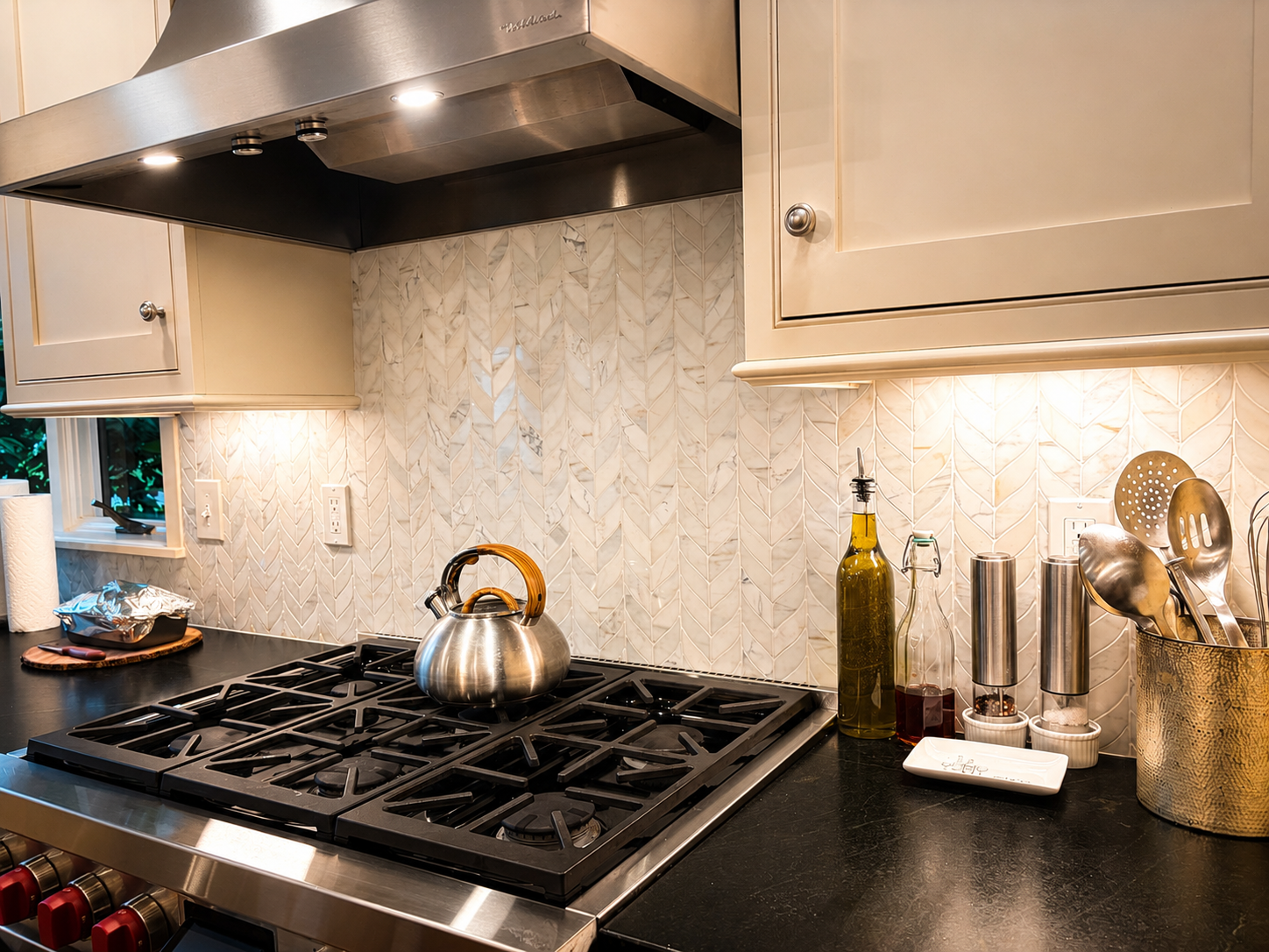 Bright renovated kitchen with a stainless range hood, tiled backsplash, gas cooktop, and dark countertops